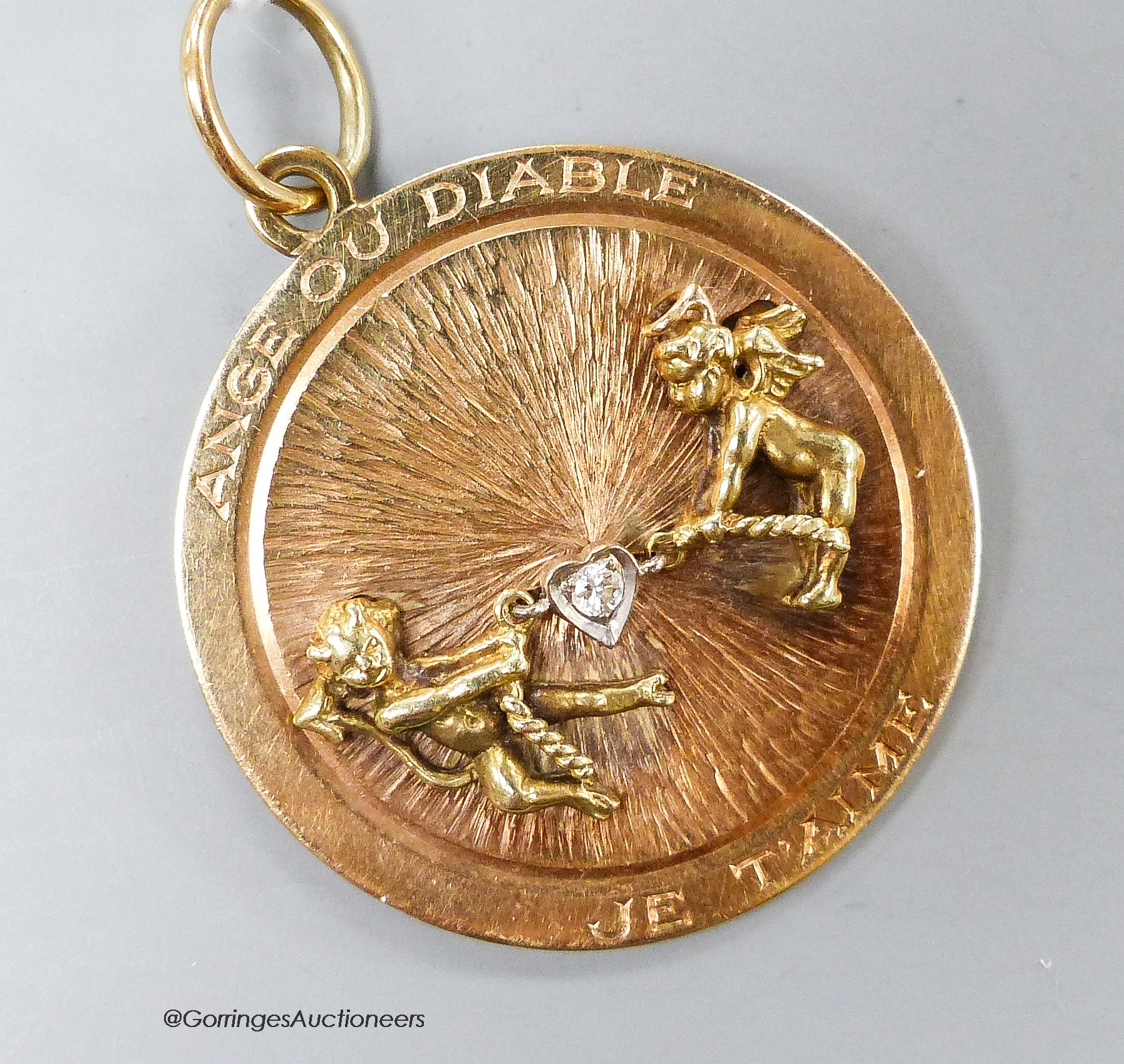 A 14k yellow metal and diamond set circular pendant, depicting articulated figures of an angel and devil in a tug-o-war and inscribed 'Ange ou Diable Je Taime', 33mm, gross 12.9 grams.